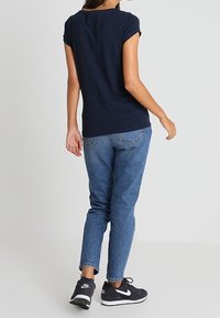 Granatowy top z krótkim rękawem, dopasowany fason. W połączeniu z jasnoniebieskimi dżinsami i czarnymi sportowymi tenisówkami. Codzienny wygląd, minimalne zdobienia.