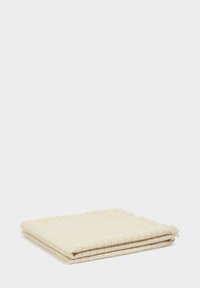 Coperta in cotone intrecciato di colore crema, con un motivo testurizzato e bordi frangiati, piegata ordinatamente e dall'aspetto morbido e soffice.
