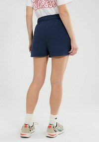 Dunkelblaue Sportshorts mit einem elastischen Bund, glatter Textur und entspannter Passform, kombiniert mit neutralfarbenen Sneakers und weißen Socken.