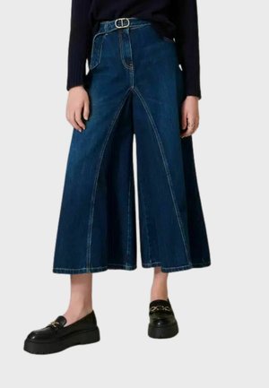 Culottes de mezclilla de pierna ancha en azul oscuro con detalle de costura frontal y una cintura alta. Combinados con mocasines de plataforma negros.