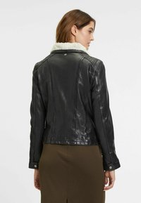 Zwarte leren jas met een schapenvachtkraag, getailleerd ontwerp, zichtbare stiksel details en zilveren knoopaccenten bij de manchetten.