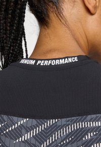 Maglietta sportiva nera con texture a coste, cuciture piatte e motivo stampato sulla parte inferiore. Logo "Venum Performance" sul colletto.