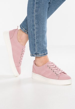Jasnoróżowe dzianinowe sneakersy z fakturowaną cholewką, wyposażone w srebrne przelotki, białą gumową podeszwę i sznurowadła. Zestawione z niebieskimi dżinsami.