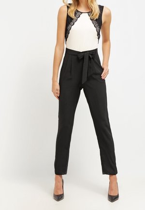 Pantalones negros de corte ajustado con cintura alta y lazo, combinados con una blusa blanca con un borde de encaje negro en los hombros.