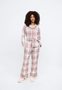 Conjunto de pijama de cuadros en crema, rojo y azul. Camisa de botones con mangas largas y pantalones a juego. Material de algodón, corte relajado, logotipo "TOMMY" en la cinturilla.