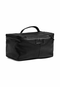 Fekete bőr kozmetikai táska cipzárral, felső fogantyúval és téglalap alakú formával. Az elején diszkrét, dombornyomott logó található.