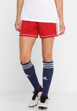 Person wearing red athletic shorts, navy knee-high Adidas socks with white stripes, and white cleats, standing against a plain background.