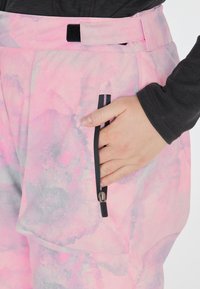Rosa und graue gemusterte Skihosen mit einer seitlichen Reißverschlusstasche und einem Klettverschluss am Bund. Der Stoff hat eine glatte Textur.