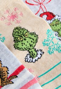 Pletené ponožky so živými vzormi; postava Grincha v zelenej, ružové snehové vločky, červené mašle a prúžkované akcenty v pastelových odtieňoch. Jemná textúra.