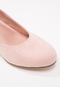 Ballerine en daim rose doux avec bout arrondi et doublure intérieure lisse, photographiée sur fond blanc.