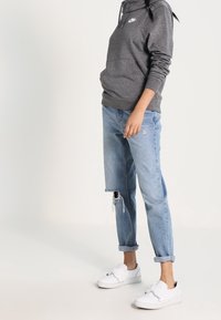 Grå Nike-hoodie med ficka fram, slitna ljusblå jeans och vita slip-on skor. Avslappnad outfit med loose fit och upprullade ärmslut.