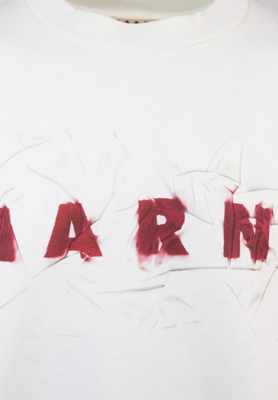 Sweatshirt en coton blanc avec des lettres rouges en détresse. Le tissu présente des plis visibles et un design à col rond.