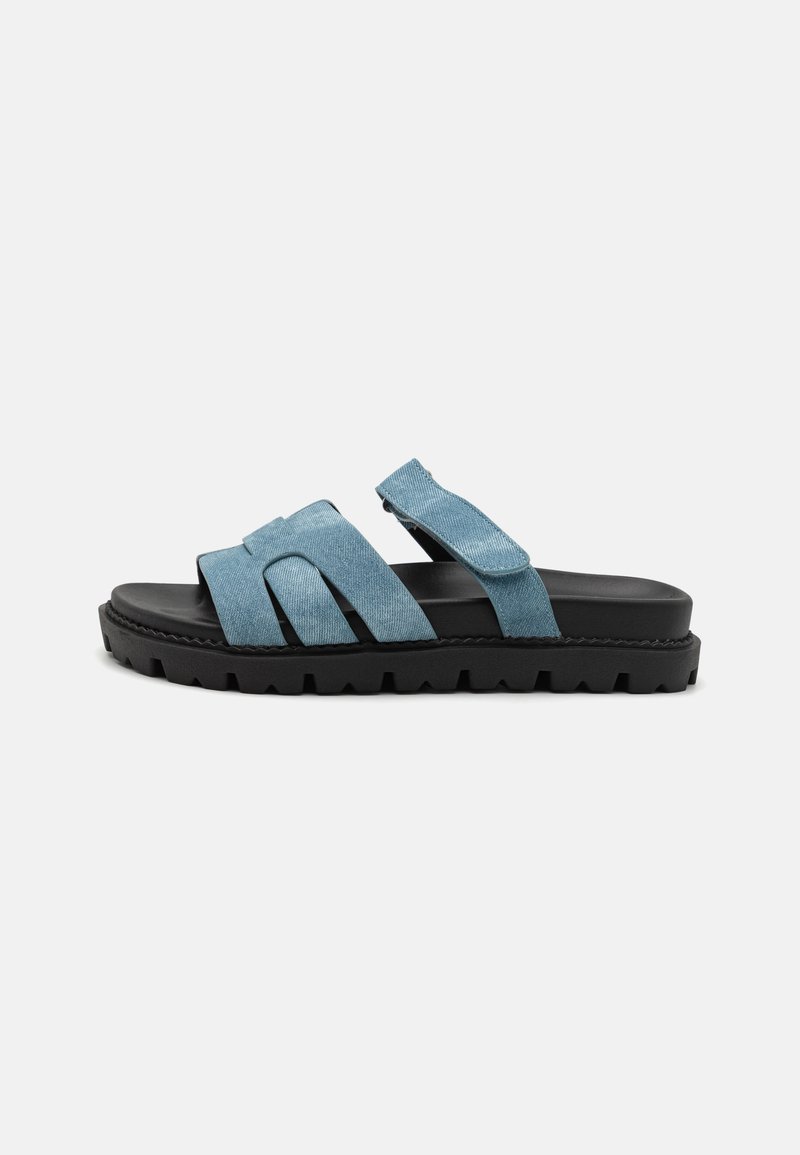 Blue fabric slide sandals with two wide straps and black rubber sole featuring zigzag tread. Edges are stitched, with adjustable fastener.