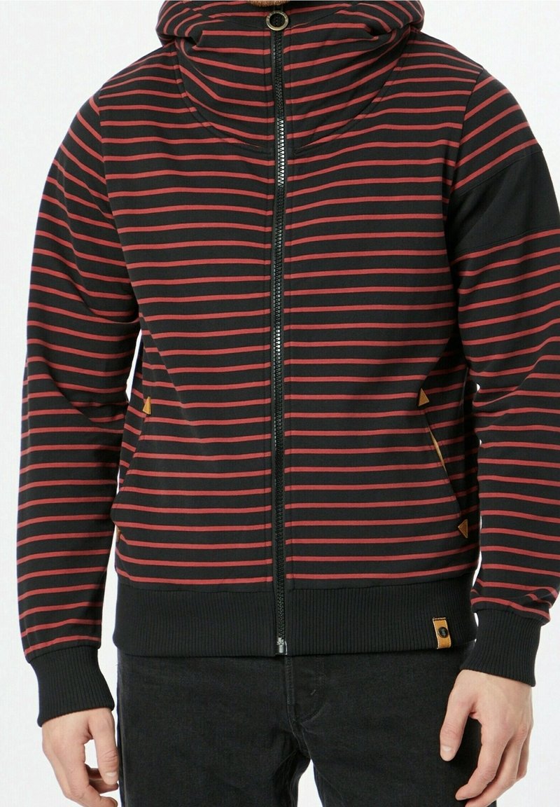 Sudadera con capucha a rayas negras y rojas, con cuello alto, cremallera frontal y puños elásticos. Presenta pequeños detalles en color beige en los bolsillos y el dobladillo.