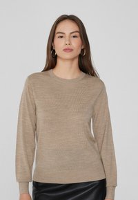 Suéter beige de manga larga con cuello redondo, de textura suave y puños acanalados, combinado con una falda de cuero negra.