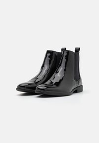 Bottines Chelsea en cuir verni noir avec une finition lisse, des panneaux latéraux élastiques, un bout arrondi et de petites languettes à l'arrière pour un enfilage facile.