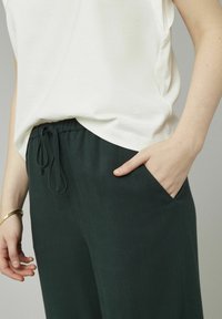 T-shirt léger en crème associé à un pantalon vert foncé à taille élastique avec cordon de serrage et poches latérales, présentant une texture lisse.