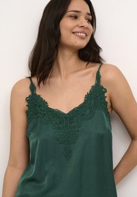 Temnozeleni satenski top s čipkastim detajliranjem pri ovratniku, z ozkimi naramnicami in gladko teksturo.