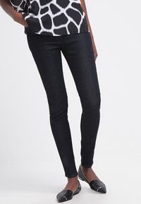 Smal jeans i mörk denim, med en slät textur och en åtsittande design. Matchas med en svart och vit mönstrad topp och svarta ballerina.