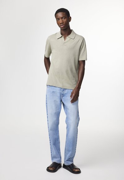 Polo shirt verde chiaro a maniche corte, abbinato a jeans di denim blu chiaro e sandali neri. Texture liscia, vestibilità casual.