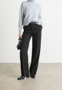 Lichtblauwe, geribbelde trui met col, gecombineerd met zwarte, op maat gemaakte broeken met wijde pijpen. Zwarte riem, gestructureerde handtas en enkellaarsjes.