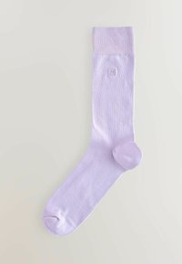 Lila rebrasta nogavica z ojačenim prstom, gladko teksturo in majhnim logotipom izvezenim blizu vrha. Narejena je iz mehkega, raztegljivega materiala.