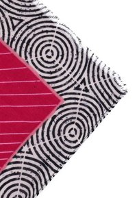 Tessuto multicolore con audaci cerchi concentrici neri e forme a diamante rosa con strisce bianche; texture morbida e bordi sfrangiati.