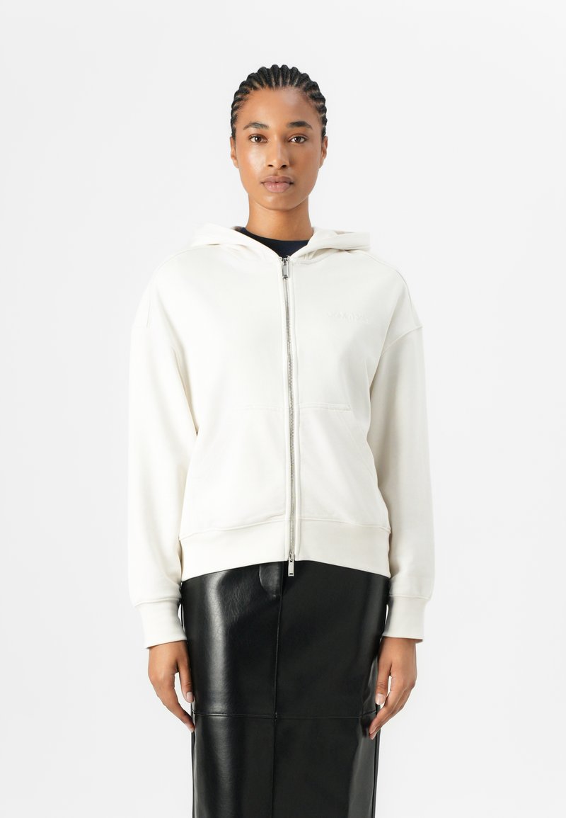 Felpa crema con zip, dotata di un grande cappuccio, tasche frontali e polsini a coste, abbinata a una gonna in pelle nera per creare un contrasto.