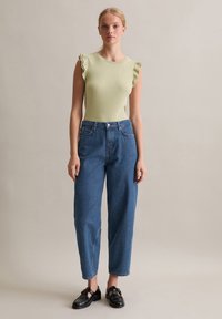 Jasnozielony ryflowany top na ramiączkach z falbanami, w zestawieniu z wysokim stanem niebieskich dżinsów i czarnymi loafersami. Prosty design, casualowy krój.