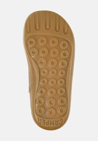 Suela de zapato marrón claro con textura de agarre redonda, que presenta patrones circulares elevados y un borde texturizado. Logotipo "Camper" impreso en la parte inferior.