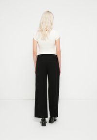 Pantalones negros de pierna ancha hechos de tela suave, con una cintura alta y dos bolsillos traseros. Combinados con un top blanco ajustado de canalé.