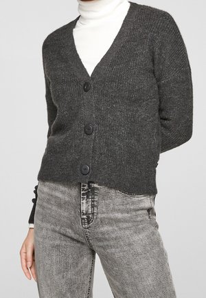Gray knitted cardigan with a v-neck, featuring four black buttons, ribbed texture, and a cropped design. Worn over a white turtleneck.
