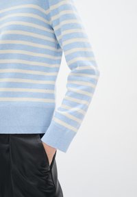Maglione azzurro chiaro lavorato a maglia con strisce orizzontali bianche, dotato di un bordo e polsini a costine. Abbinato a pantaloni in pelle nera.