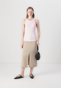 Světle růžový ribbed top bez rukávů, béžová midi sukně s předním rozparkem a černé špičaté baleríny. Kabelka je černá s zakřiveným designem.