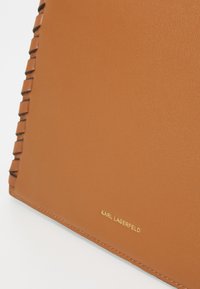 Brown leather handbag with a textured surface, featuring braided accents on one side and a metallic gold logo inscription.