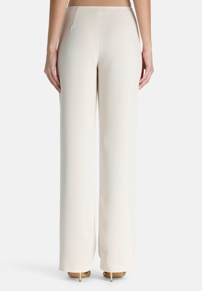 Un pantalon large crème présente une texture lisse et satinée, avec une taille haute, des plis subtils et une silhouette épurée et élégante.