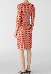Robe rouge avec un motif géométrique crème répétitif, manches trois quarts, taille ajustée, longueur genou et encolure ronde.