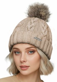 Tan knitted beanie with a ribbed cuff, cable knit pattern, and a faux fur pom-pom on top. Features a small silver logo plaque.