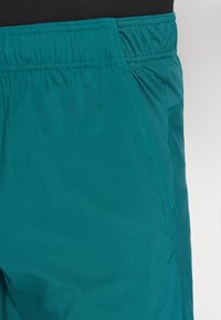 Shorts teal avec une taille élastique, texture lisse, poches latérales et tissu léger pour le confort et la mobilité.