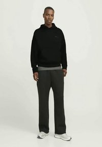 Juodas džemperis su gaubtu su mažu logotipu, derinamas su tamsiai pilkomis kelnėmis. Kelnės yra laisvo stiliaus. Avalynė – šviesiai pilki sportbačiai. Minimalistinis dizainas.