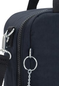 Tmavě modrá textilní taška s hladkým povrchem, obsahující zip, stříbrné kovové prvky a očko na klíče. Kompaktní design se silnými popruhy.