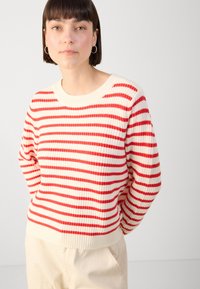 Röd och gräddfärgad randig stickad tröja med rund halsringning och ribbade ärmslut och nederkant. Mjuk textur med en lös och avslappnad passform.