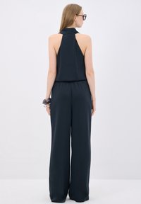 Navyblå, ärmlös jumpsuit med hög krage och elastiskt midjeband; bred bendesign ger en löst passform. Sidenliknande, slät textur.