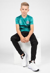 Turquoise short-sleeve sports shirt with black stripe, logo, and black athletic pants. White sneakers with black accents.