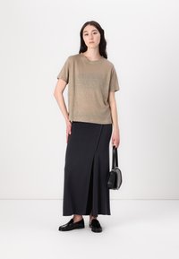 Beżowy t-shirt z krótkim rękawem, połączony z czarną spódnicą maxi z bocznym rozcięciem. Stylizację dopełniają czarne loafersy i mała torebka.