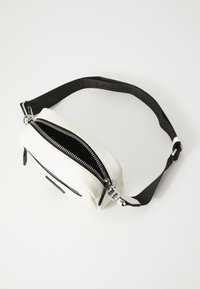 White faux leather bag with two zippers, black lining, and adjustable black strap featuring embossed text. Compact, rectangular shape.