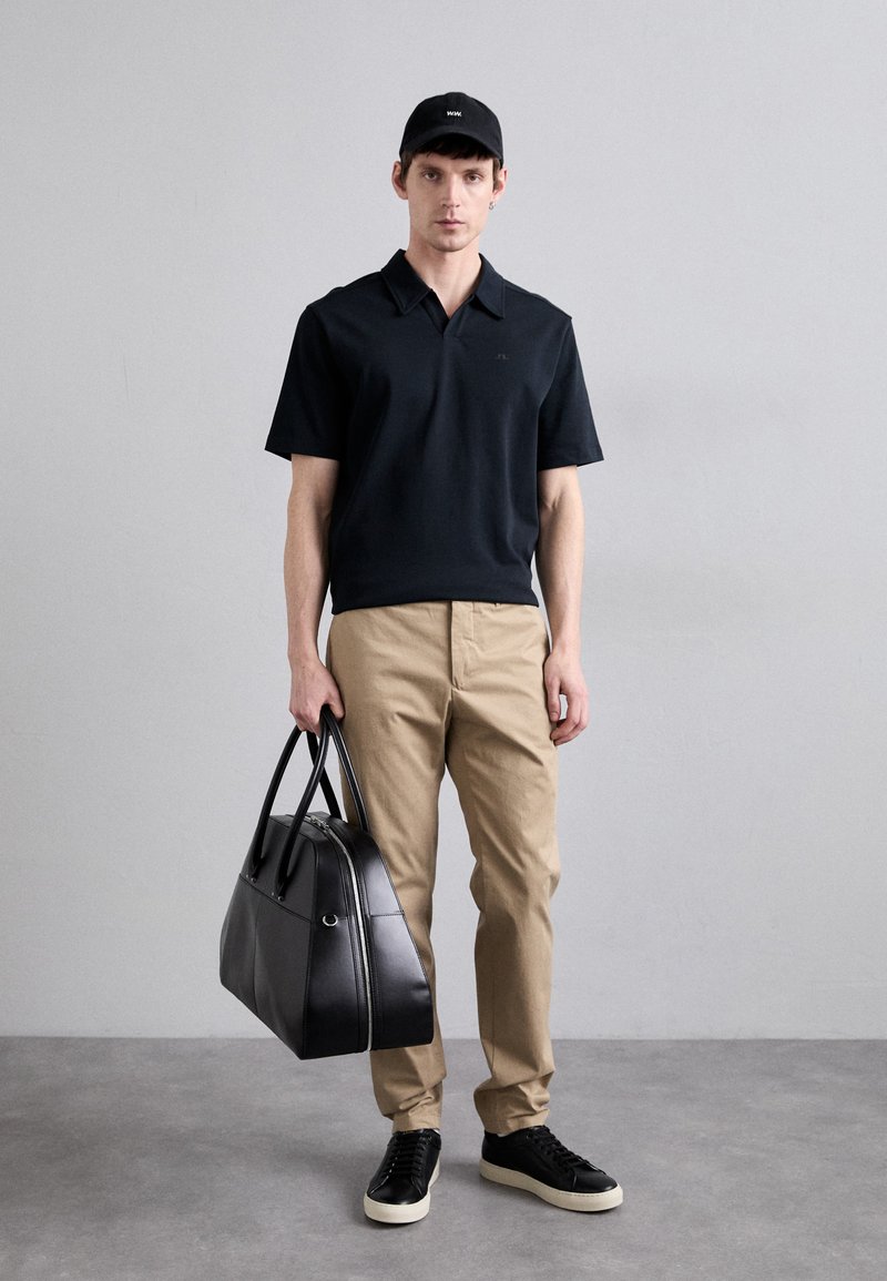 Svart polo skjorta, beige byxor, svarta sneakers och en stilren svart läderväska med dubbla handtag. Slät textur, minimalistisk design.