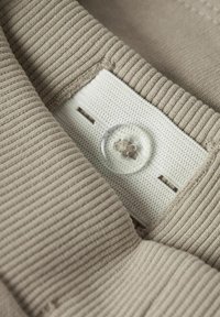 Tissu beige côtelé avec une étiquette blanche comportant un bouton et des détails de couture. Bouton transparent avec un motif de fleur sur l'étiquette.