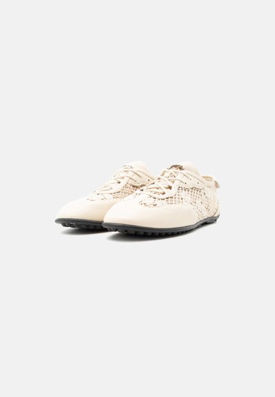 Ζευγάρι μπεζ παπούτσια με κορδόνια, με πλευρές από πλεκτό διχτυωτό και μαύρες ελαστικές σόλες, εμφανίζεται από την μπροστινή αριστερή γωνία σε λευκό φόντο.