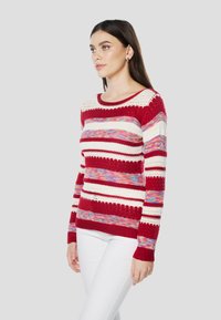 Rood-wit gestreepte gebreide trui met verschillende patronen, voorzien van lange mouwen en een ronde halslijn. Gemaakt van zachte stof met textuurrijke accenten.